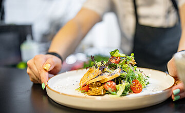 Catering: Person stellt einen Teller auf einen Tisch mit einem hübsch angerichteten Sommersalat