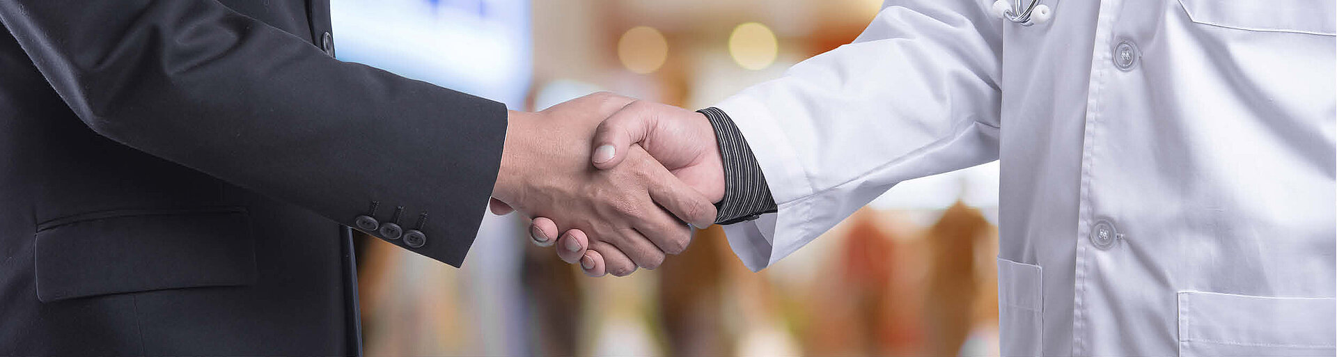 Servicegesellschaften: Bild zeigt einen Handschlag zwischen einer Person im Anzug und einer Person im Arztkittel