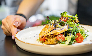 Catering: Person stellt einen Teller auf einen Tisch mit einem hübsch angerichteten Sommersalat