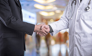 Servicegesellschaften: Bild zeigt einen Handschlag zwischen einer Person im Anzug und einer Person im Arztkittel